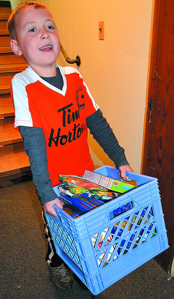 Quinn Corrigan, 5, of Oxford carries a crate of donated food to the pantry's basement.