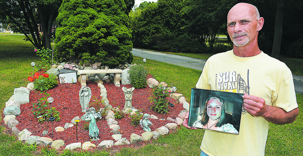 Christopher Woityra holds a photo of his late daughter Taylor Beth as he stands near the memorial garden he created in the shape of a peace sign. Photo by C.J. Carnacchio.