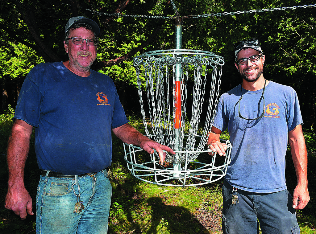 Park Superintendent Jeff Kinasz (left) and Miles Lawrence, a seasonal parks dept. worker and avid disc golfer, pose with one of the baskets that's part of the new disc golf course spread across 100 acres of Oakwood Lake Township Park. Photo by C.J. Carnacchio.