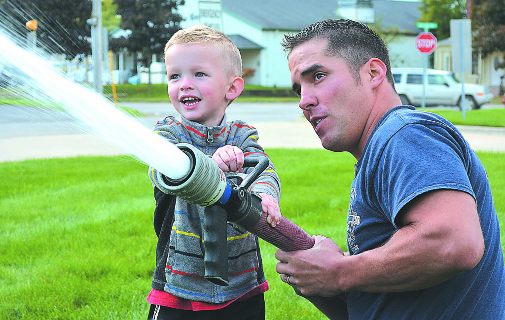 Oxford resident Vinny Halik, 2, gets to spray a real, regulation fire hose with some assistance from Oxford rookie firefighter Jesse Grenillo. Photo by C.J. Carnacchio.