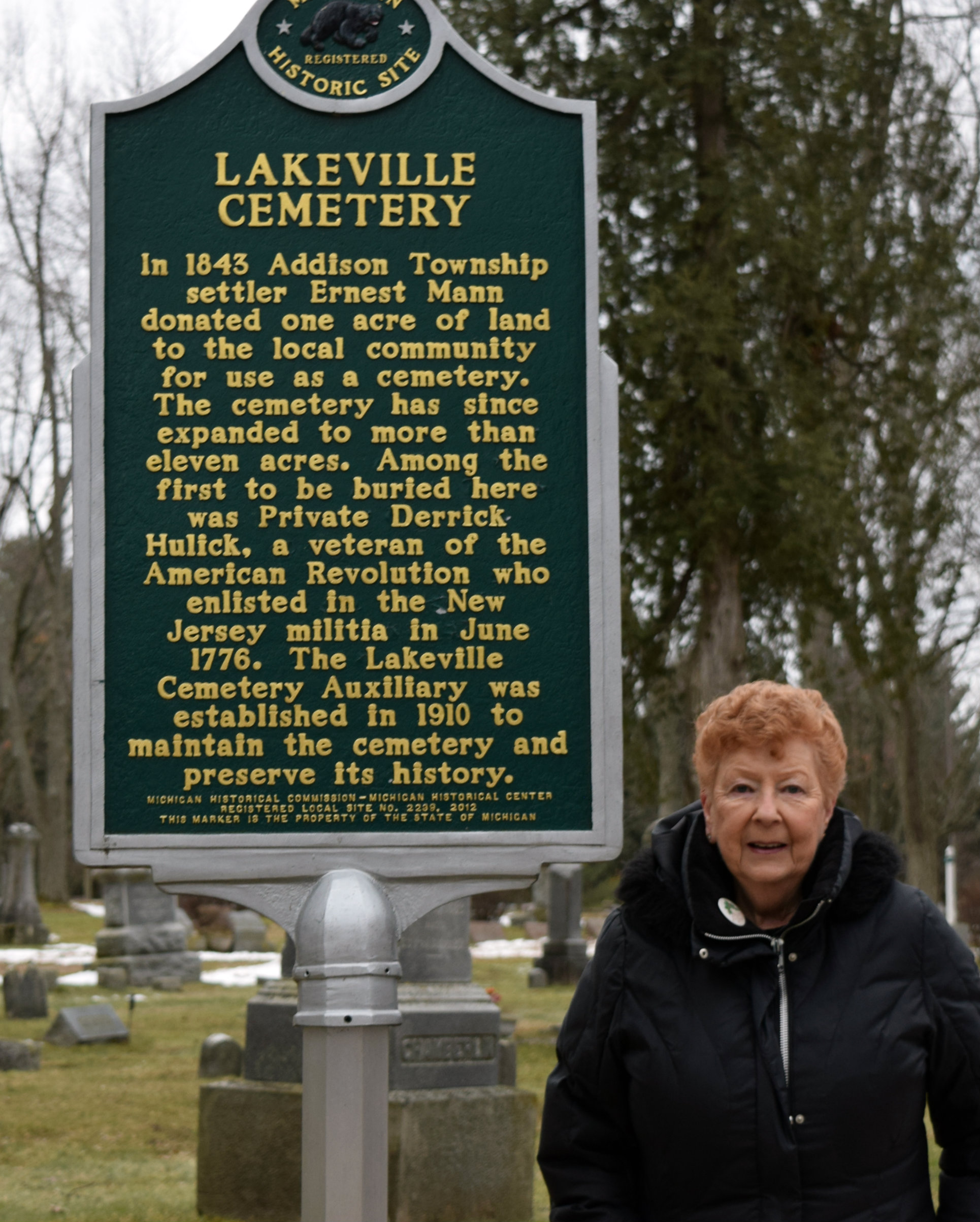 Marlene Mallia, president of the Lakeville Cemetery Auxiliary, poses next to the state historical marker. Photo by Elise Shire.