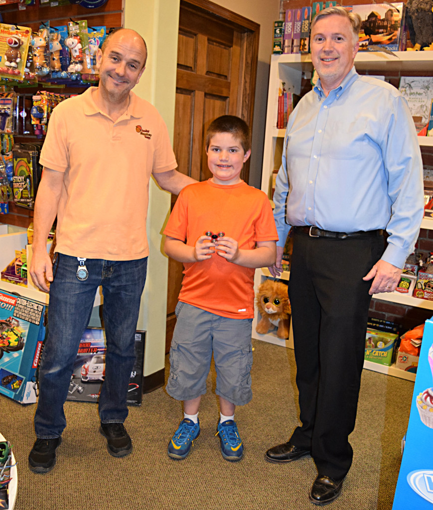 Tom Jones (from left) , owner of Funky Monkey Toys, OES fifth-grader Alex VanHaren and Greg Clay, a representative for Blessings in a Backpack. Photo by Elise Shire.