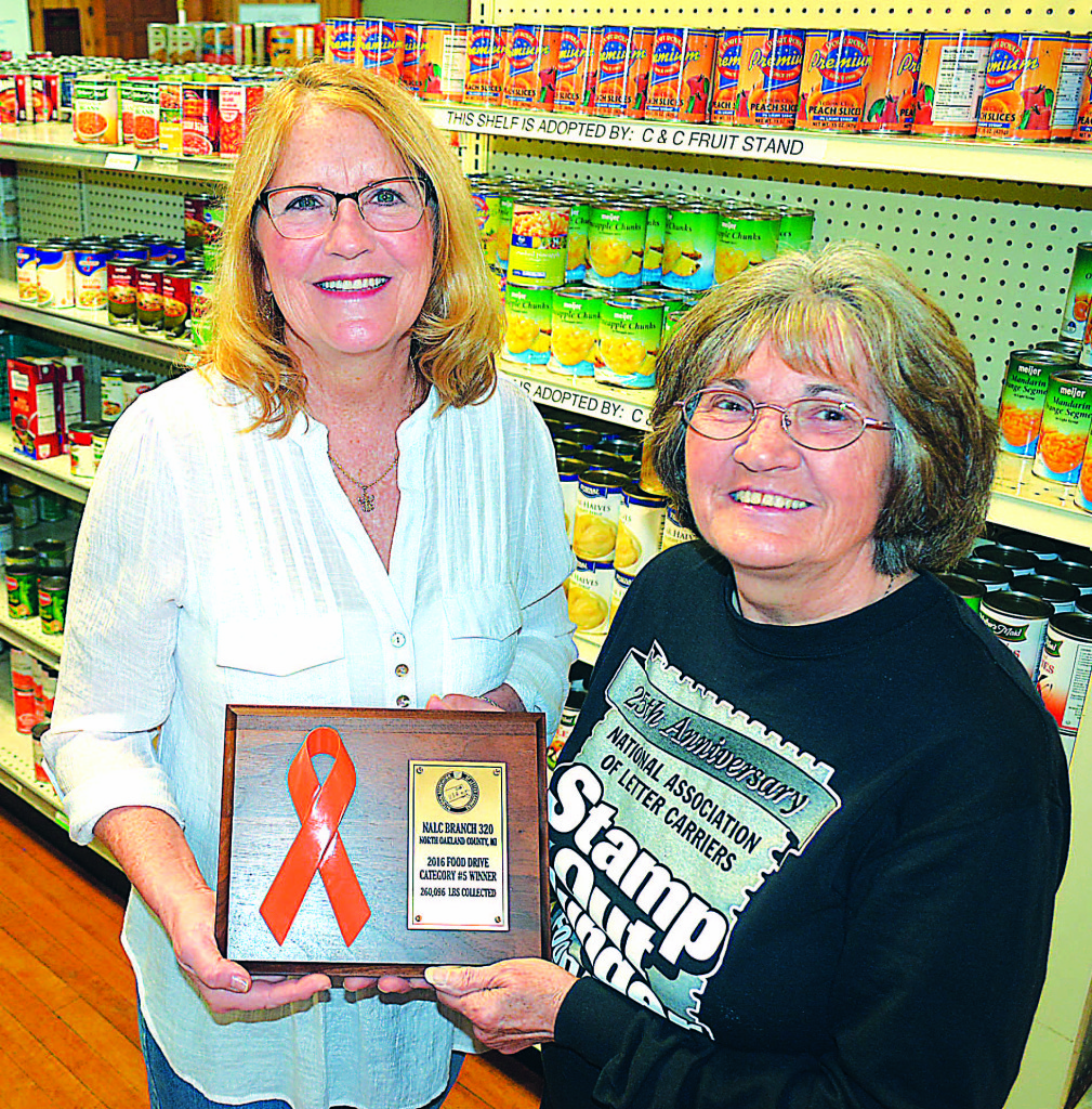 Julie Howald (left), vice president of the the Oxford-Orion FISH board, and Vicky Haist, food drive coordinator for National Association of Letter Carriers Branch 320, are encouraging folks to donate nonperishable food items as part of the 25th Annual Stamp Out Hunger drive on Saturday, May 13. Last year, Branch 320, which includes the Oxford and Lake Orion post offices, collected 260,096 pounds of food and received the plaque shown above. Photo by CJC.