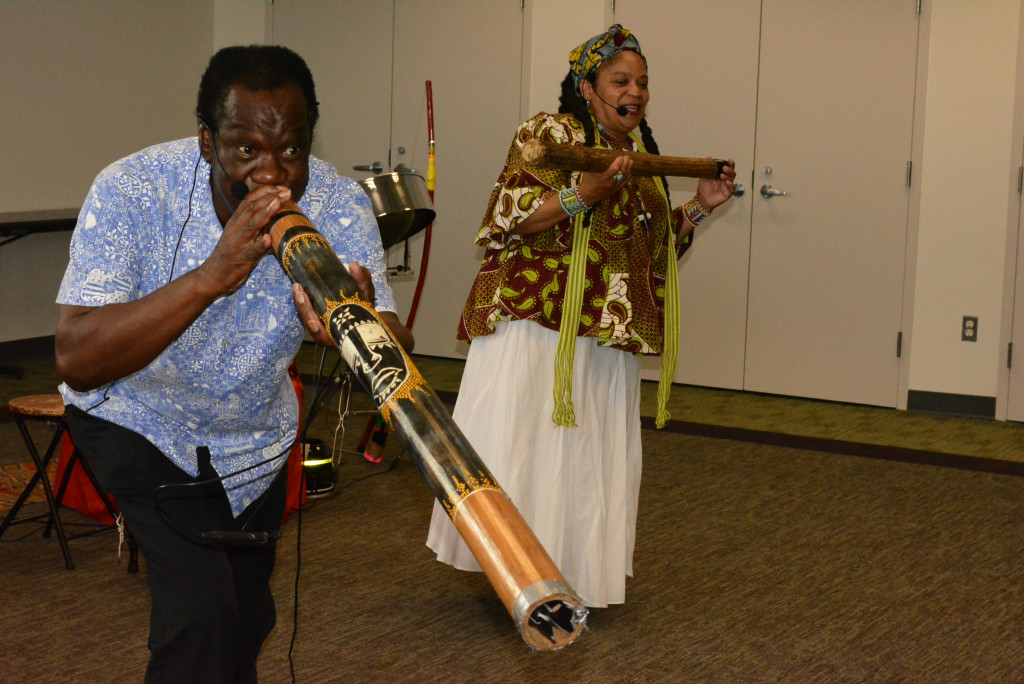 Robert Allison, plays a didgeridoo, a wind instrument developed by the indigenous peoples of northern Australia. Behind him, Audrey Allison performs with a rainstick, an instrument that originated on  the South American continent.