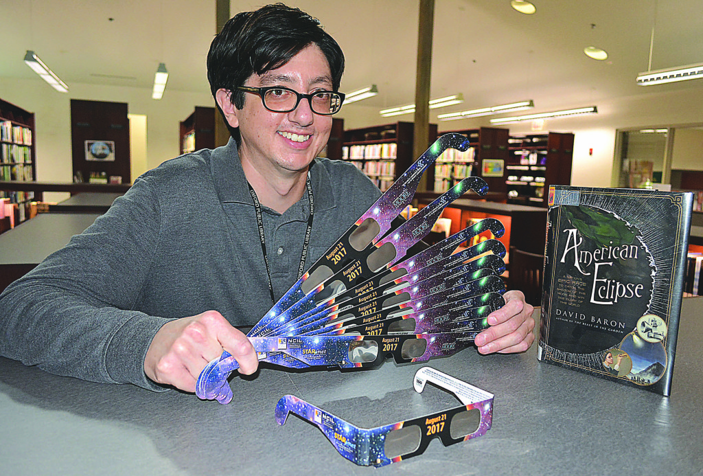 Ricardo Aguirre, a librarian assistant at the Oxford Public Library, holds a bunch of special eclipse-viewing glasses, which are available free to the public while supplies last. Photo by C.J. Carnacchio.