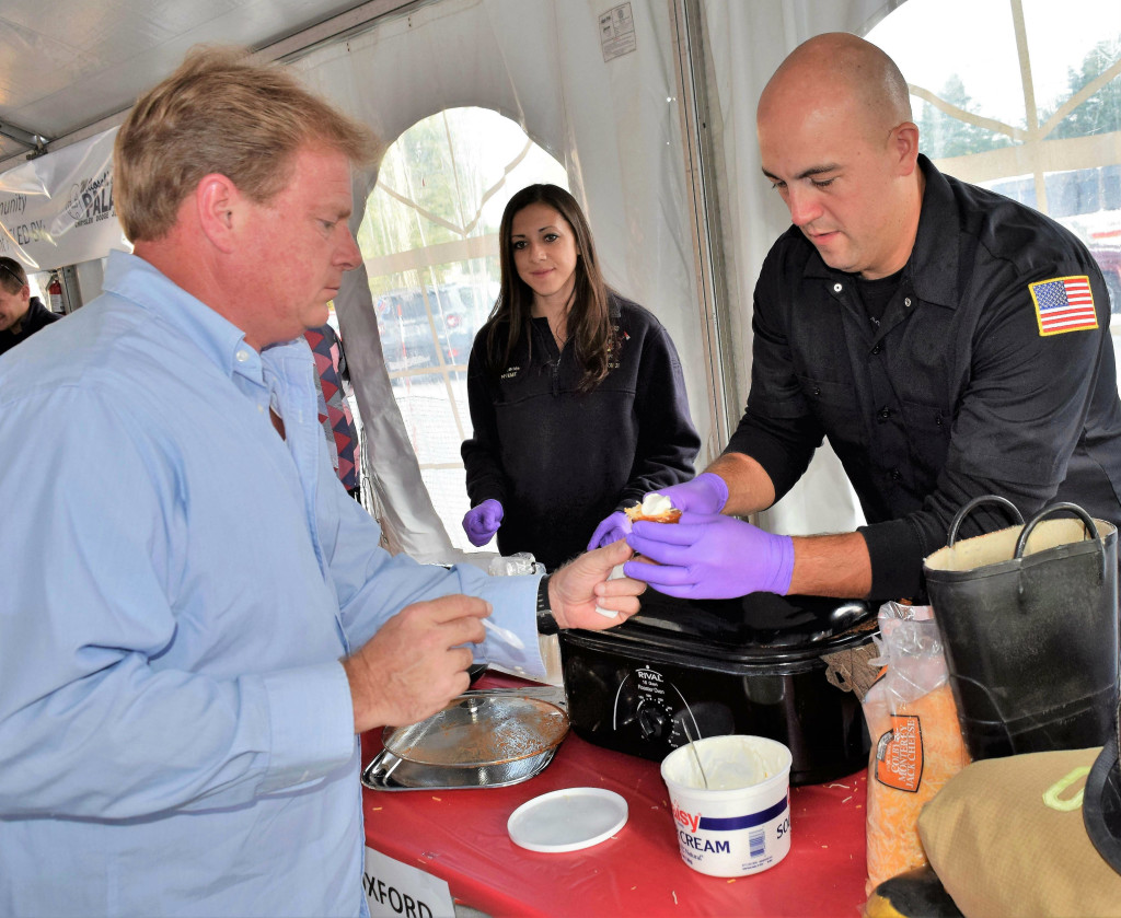 Oxford firefighter Alan Adorjan serves up a cup of chili to Rick Naughton during the Dragon on the Lake Festival in Lake Orion. Photo by Jim Newell.