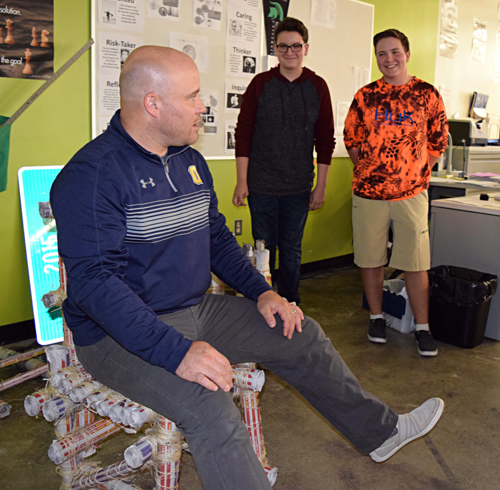OHS students A.J. Laroche (left) and Austin Couch (right) built the chair that teacher Philip Kimmel is sitting in and judging. Photos by Elise Shire.