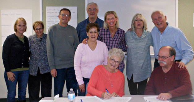 Sitting at the table with FISH President Laurene Baldwin as she signs the lease agreement is Treasurer Randy Gower.  Standing directly behind Baldwin is Sue Hackstock, office coordinator.  Other board members are (from left):  Secretary Sue Black, Judy Miller, Ron Wood, Alex Jablonowski, Michelle Behm, Lynn Kennis and Don Danko.