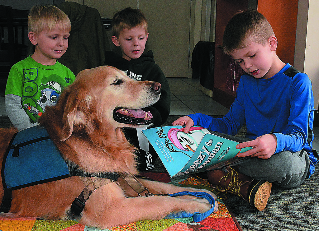 Daniel Axford first-grader Blake Curtis (far right), 7, reads a book aloud as his brothers Drew, 3, (far left) and Carter, 5, listen with Charley, a therapy dog. Photo by C.J. Carnacchio.