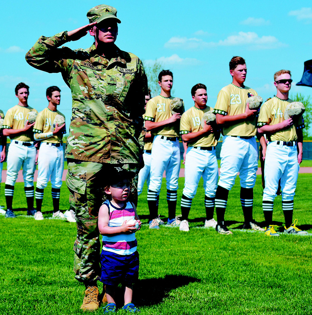 Sgt. Johnna Kovach salutes during the playing of the National Anthem. Behind her is the Oxford High School varsity baseball team. Looking on is her young son, Collin.