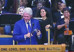 Former U.S. President Bill Clinton uses his smartphone to play the 1968 hit song “Think” during Aretha Franklin’s funeral at Detroit’s Greater Grace Temple. Seated behind him to the immediate right is Oxford Schools orchestra director Natalie Frakes, who performed at the Aug. 31 funeral with the Aretha Franklin Orchestra. Image courtesy of WXYZ-TV Detroit.