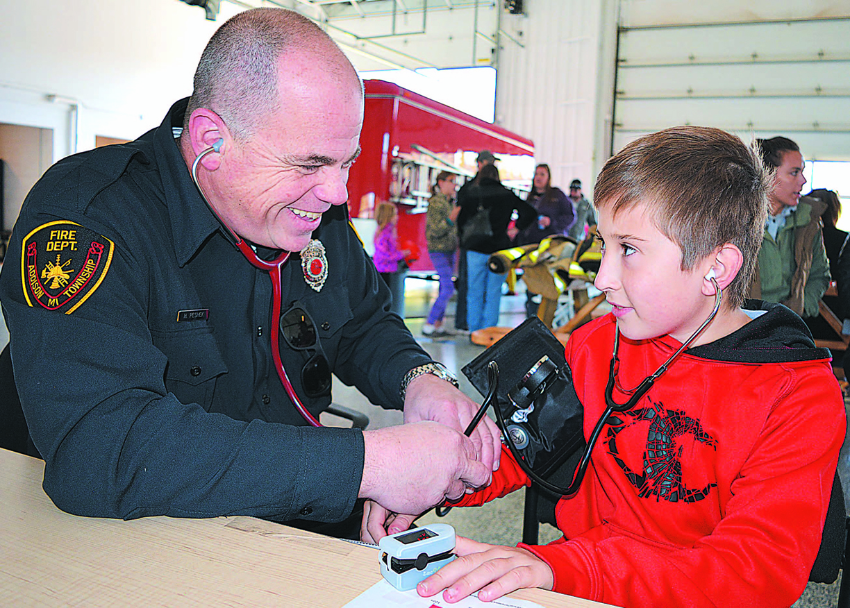 Addison Firefighter Heathen Peshe (left) measures 10-year-old Almont resident Dillan Lindberg’s blood pressure and helps him listen to his heartbeat. Photo by C.J. Carnacchio.