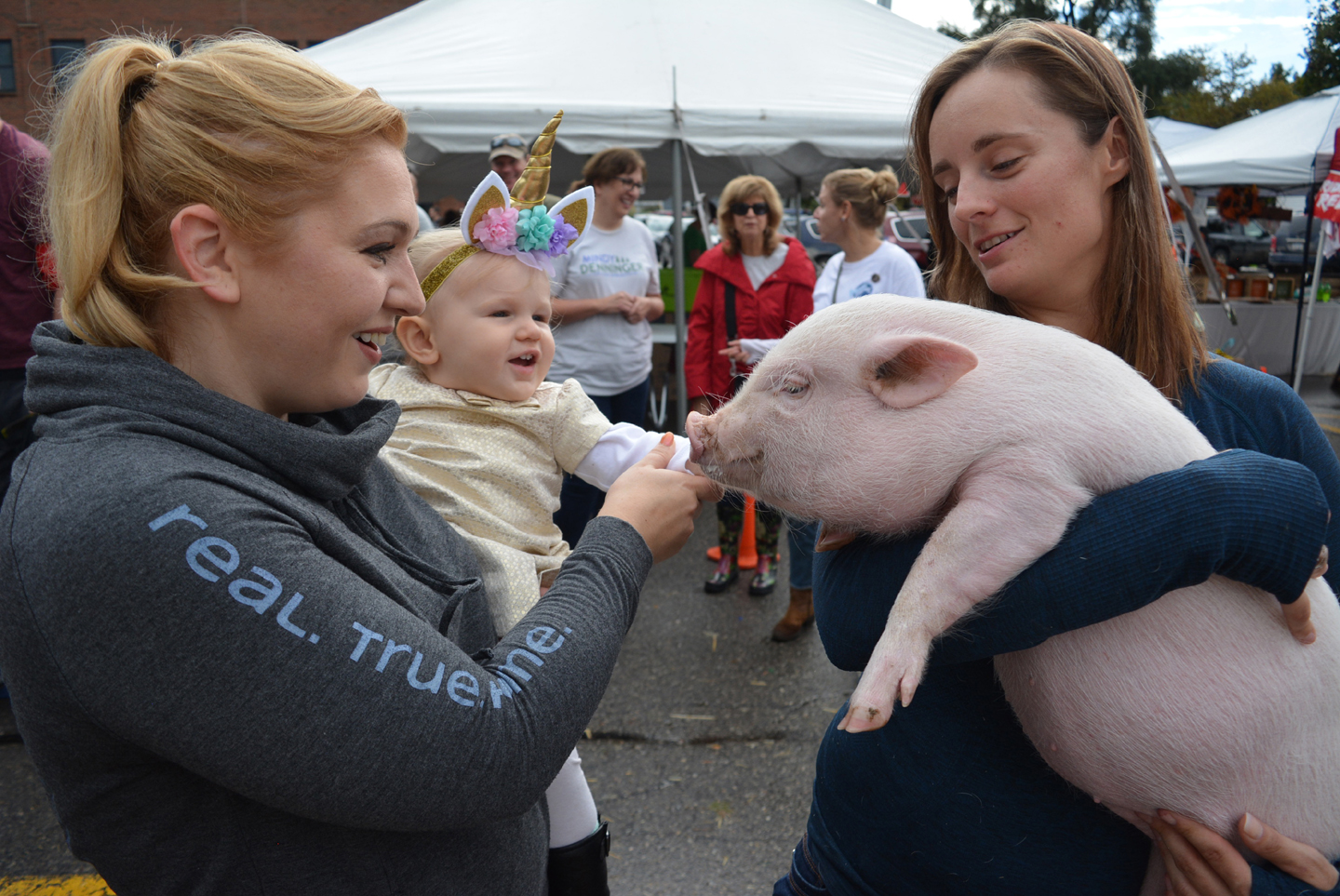 Oxford resident Meagan Brandt (left) and her daughter Brynna, 1, meet Bubbles the Pig, who won the pet costume contest by dressing as a “streaker.” Bubbles’ owner is Jessica Filiatrault (right), owner of Matador Farm in Oxford. Photo by C.J. Carnacchio.