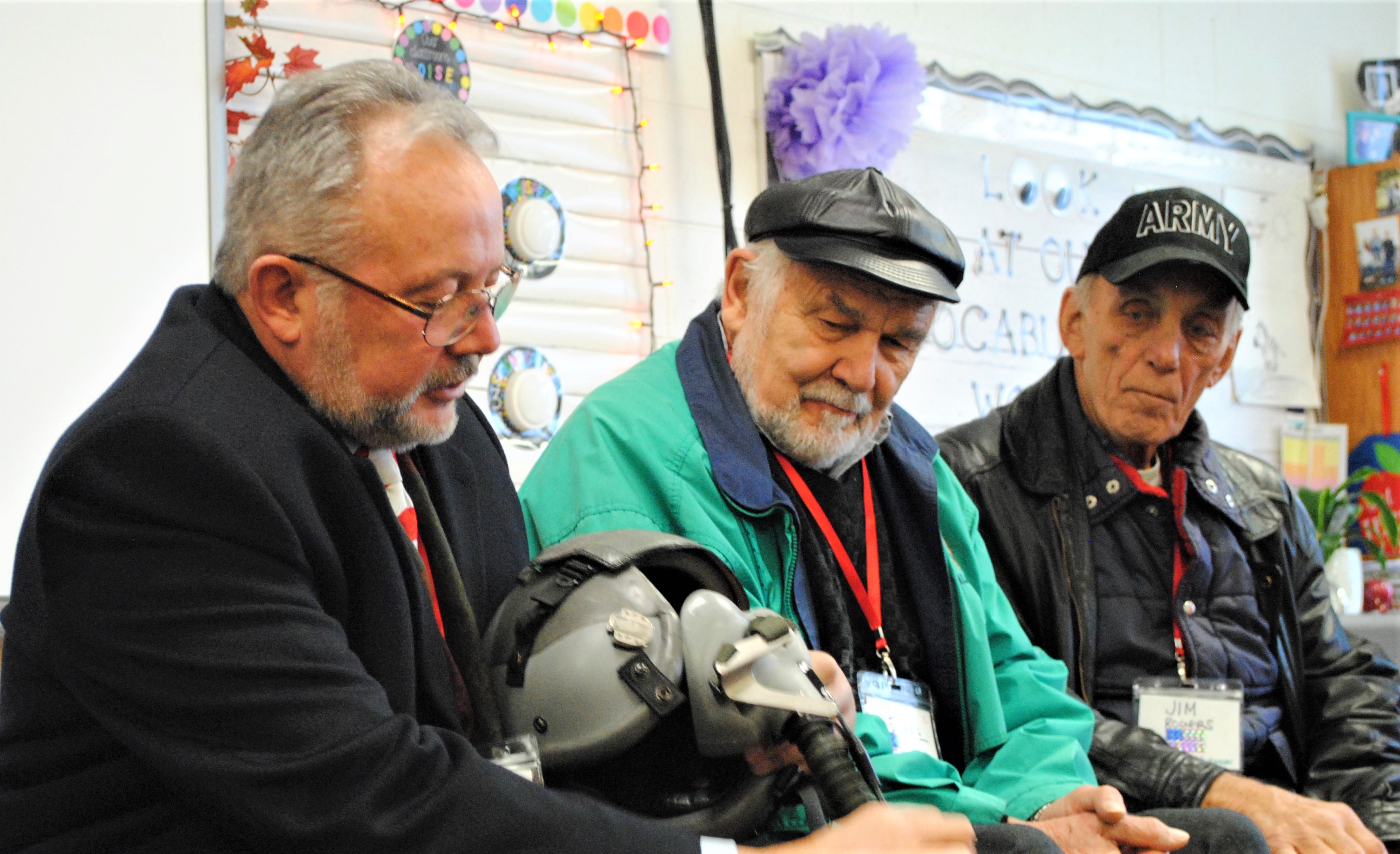 While some came with memories, others came with mementoes from their time in the service for students to see. Greg Gonyea had his air helmet and parachute pack in tow for a class of second-graders to put their hand on. With him is veterans Lloyd Schmaltz and Jim Rogers. Photo by Shelby Tankersley.